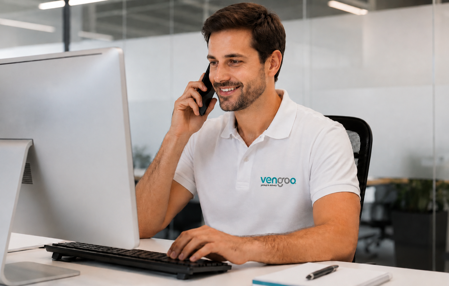 Atención al cliente para transporte urgente en Barcelona | Vengoo Empleado de Vengoo atendiendo una llamada de transporte urgente en Barcelona desde una oficina moderna mientras trabaja frente al ordenador.